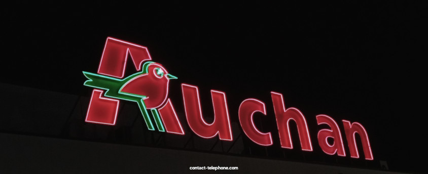 Lettres éclairées d'une enseigne Auchan placées sur le toit d'un supermarché, brillant dans la nuit.