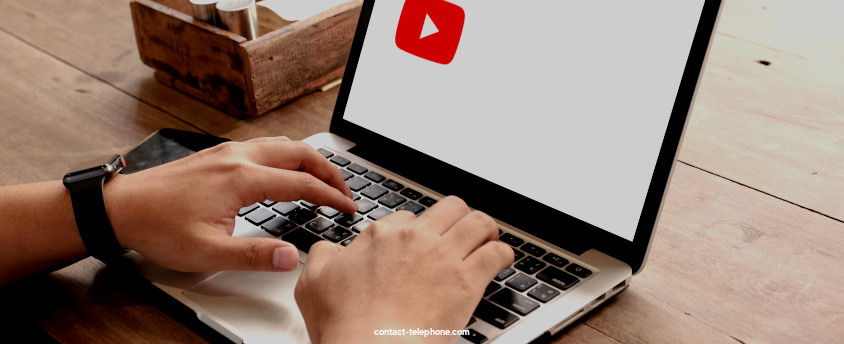 Mains d'un homme tapant sur le clavier d'un ordinateur portable devant un écran affichant le logo de YouTube.