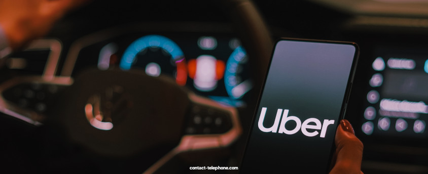 Téléphone mobile affichant Uber tenu dans une main dans un véhicule VTC, devant le volant et le tableau de bord.