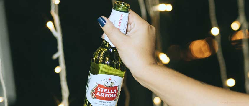 Main de femme portant une bouteille de bière Stella Artois.